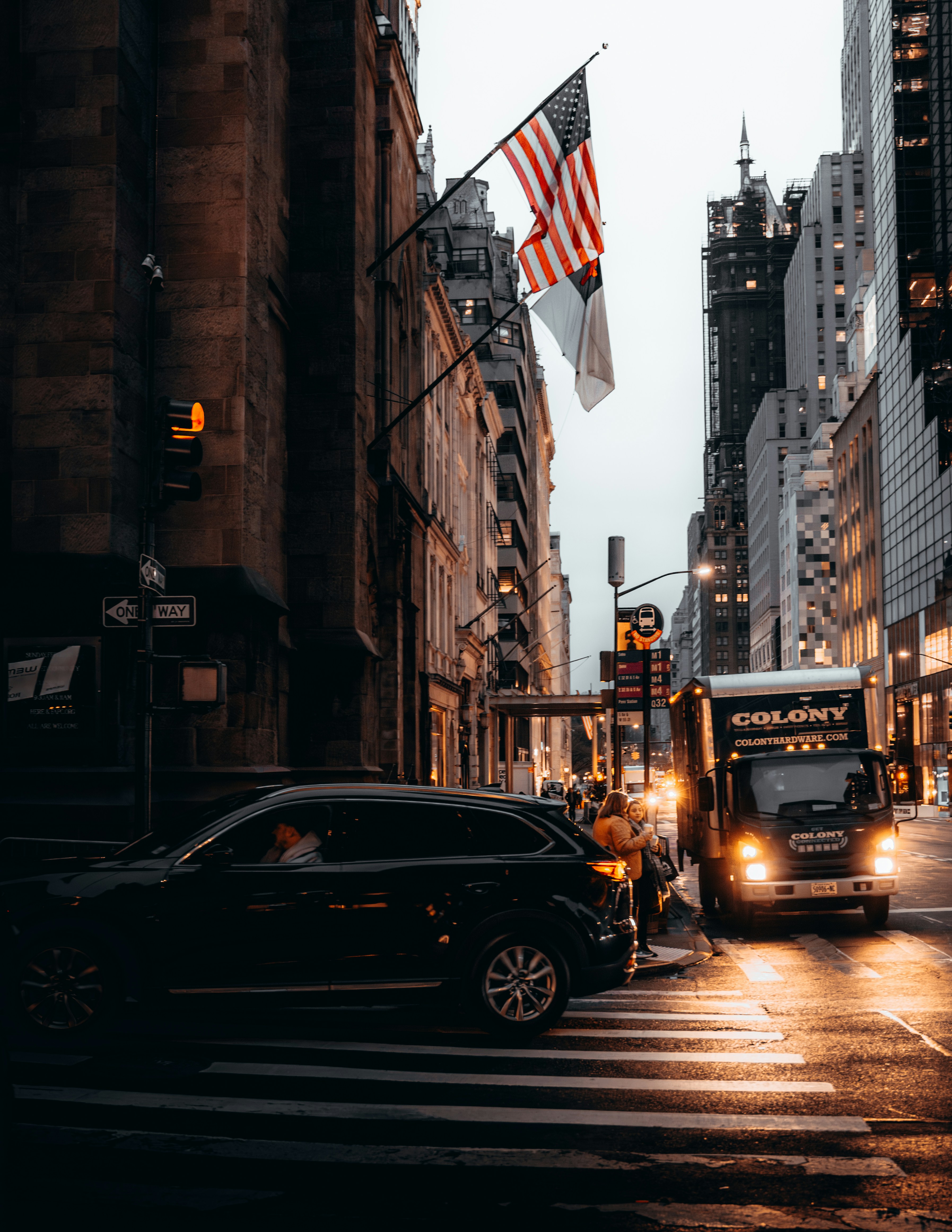 A sleek black car is the centerpiece of this atmospheric photo. The setting is early morning, but darkness still lingers, with streetlights casting a warm glow on the pavement.
